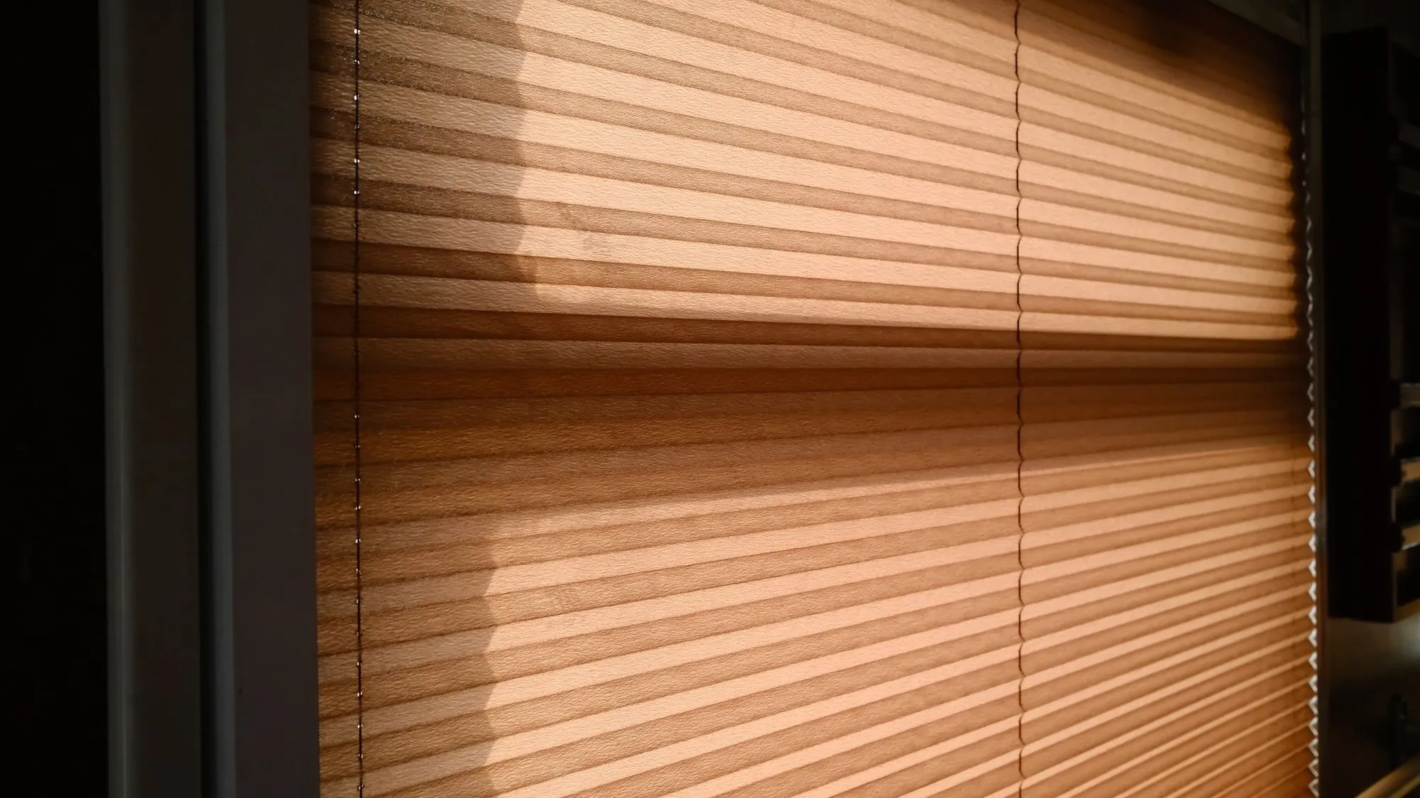 Warm sunlight falls across the pleats of a closed window blind.